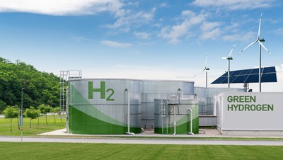 Large cylinder metal tanks with a green H2 painted on the left and green hydrogen written on a white building on the right. 